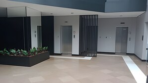 A modern lobby with a central planter, two elevators, and a minimalist design. - Saint Sebastian ap101-stúdio  (Jaragua do Sul)