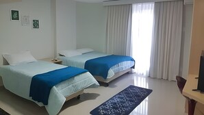 A hotel room with two beds, a small table, a bench, and a TV. - Saint Sebastian ap101-stúdio  (Jaragua do Sul)