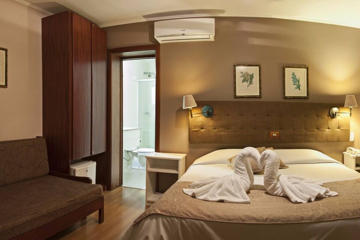Una habitación de hotel con cama, dos mesitas de noche, un sofá y una puerta que da a un baño.