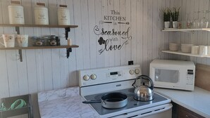 Et køkken med komfur, mikroovn og hylder med køkkenudstyr.