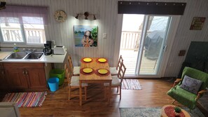 A cozy kitchen with a dining table set for four, wooden cabinets, a green chair, and a view of the backyard through a sliding glass door. - Relax on Benson Lake, Rideau System (Westport)