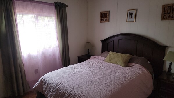 Un dormitorio con cama, mesita de noche, lámpara y ventana con cortinas.