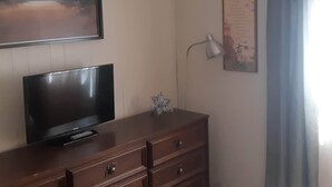 Et værelse med et fladskærms-tv på en trækommode, en vægmonteret lampe og et indramet dokument på væggen.