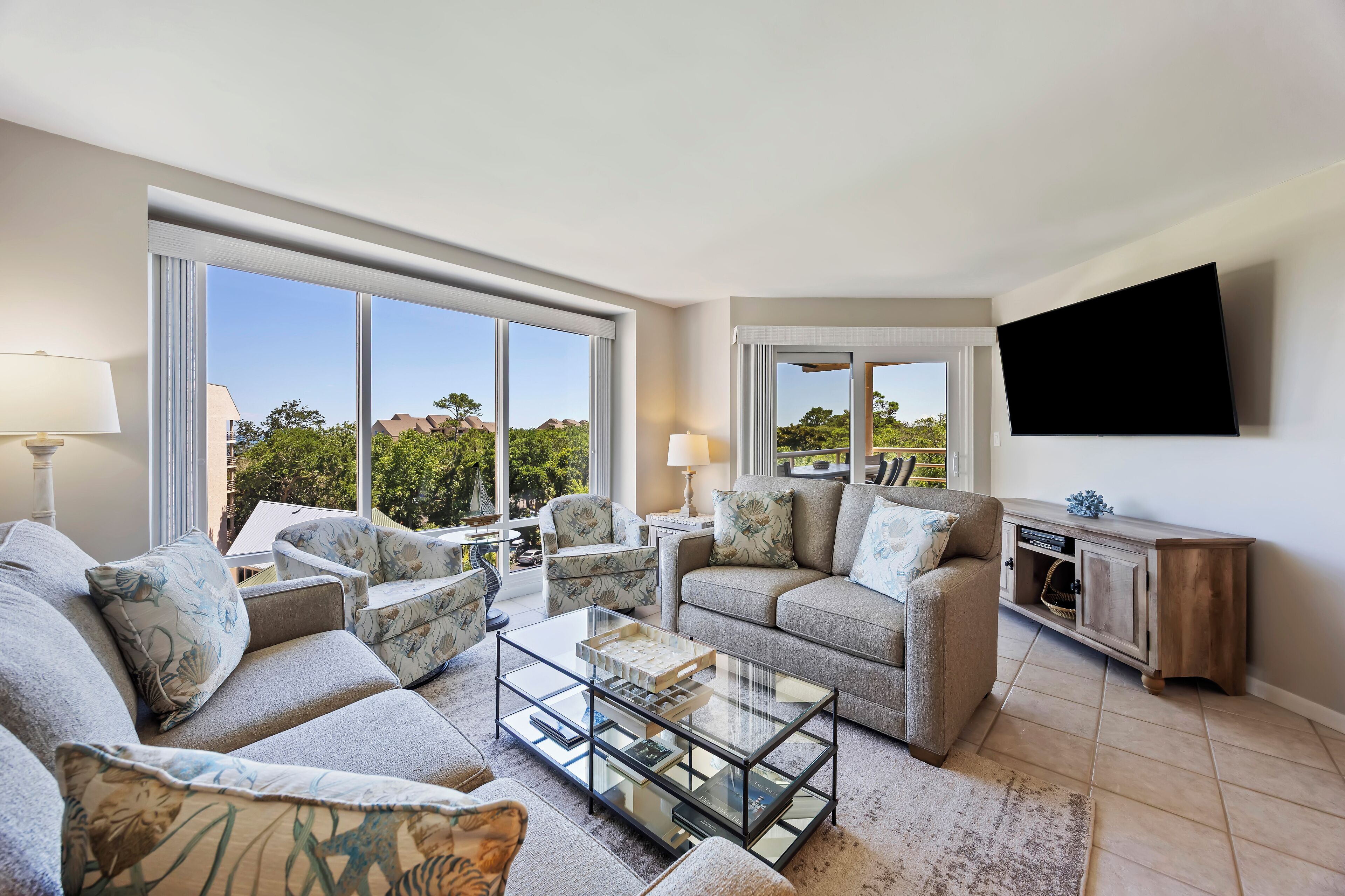 A modern living room with a sofa set, a glass coffee table, and a flat-screen TV mounted on the wall.