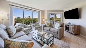 A modern living room with a sofa set, a glass coffee table, and a flat-screen TV mounted on the wall. - End Unit; Ocean Peek; 5th floor - Villamare. 2 hrs Pickleball/Tennis per day! (Hilton Head Island)