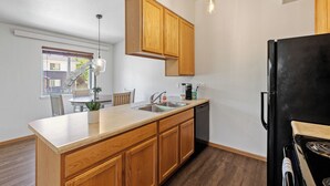 Una cocina moderna con armarios de madera, un refrigerador negro, un lavamanos y una zona de comedor con una mesa y sillas.