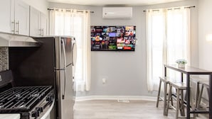 A modern kitchen with a built-in stove, refrigerator, and a flat-screen TV mounted on the wall displaying various channels. - Modern Apartment in Black Rock (Bridgeport)