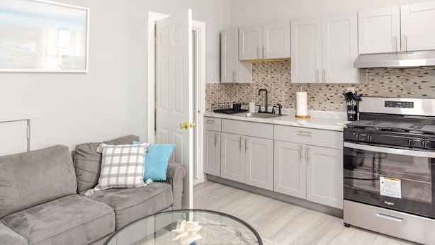 A modern kitchen with white cabinets, a black stove, and a tiled backsplash. - Modern Apartment in Black Rock (Bridgeport)