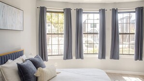 A bedroom with a large bed, grey curtains, and a view of the outside. - Modern Apartment in Black Rock (Bridgeport)