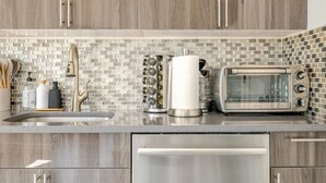 Une cuisine moderne avec des meubles de couleur grise, un lave-vaisselle en acier inoxydable, un grille-pain et un pare-feu en carreaux.