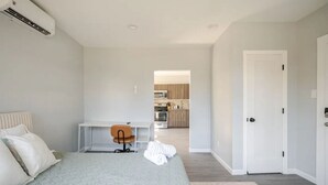 Une chambre avec un lit, un bureau et une chaise. Une porte donne accès à la cuisine.