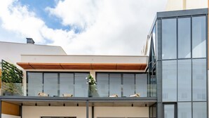 Un edificio moderno con fachada de vidrio, techo inclinado de madera y un balcón con asientos.