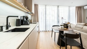 Una cocina moderna con un lavamanos, un grifo negro y una cafetera. Se ve una mesa de comedor con sillas y un sofá al fondo.