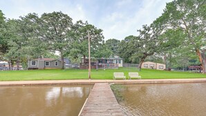 A wooden dock leading to a calm water body, surrounded by green lawns and trees. - Lakefront Gun Barrel City Home w/ Dock & Deck (Gun Barrel City)