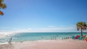 Une plage avec un ciel dégagé, une zone sablonne avec une promenade dallée et des chaises colorées.