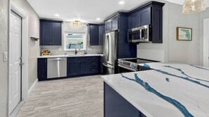 Une cuisine moderne avec des meubles bleu foncé, des appareils en acier inoxydable et un plan de travail en marbre.