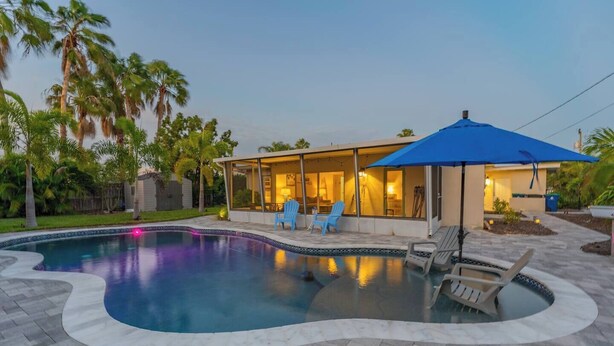 Une piscine à bord incurvé, entourée d’une terrasse avec des chaises et un espace salon abrité.