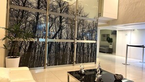 A modern lobby with a glass wall displaying a forest scene, a reception desk, and a coffee table with decorative items. - Redibuk - Luxury duplex 1BR Miraflores (Lima)