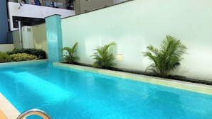 A swimming pool with a clear blue water, surrounded by a low wall and some greenery. - Redibuk - Luxury duplex 1BR Miraflores (Lima)