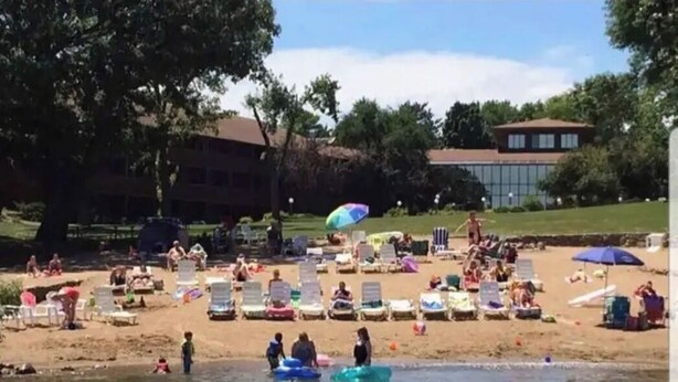 Une plage avec des chaises longues et des parasols, un espace piscine et un bâtiment en arrière-plan.