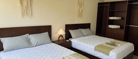Dos camas individuales con cabeceras de madera, una mesita de noche con lámpara, un armario y un aire acondicionado instalado en la pared.
