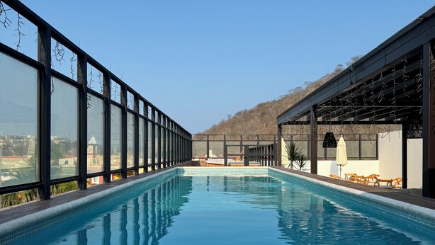 Una piscina interior rectangular con agua azul cristalina, rodeada de paredes de vidrio y vistas a un paisaje montañoso.