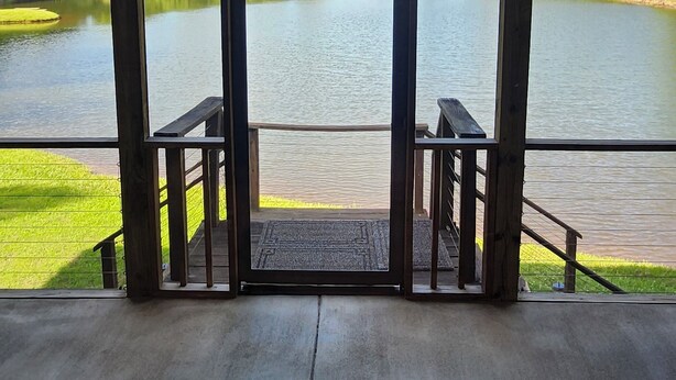 A covered viewing area with a wooden deck and a glass door leading to a lake.