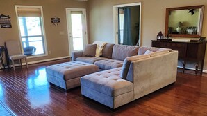 A spacious living room with a sectional sofa, hardwood floors, a ceiling fan, and a large window.