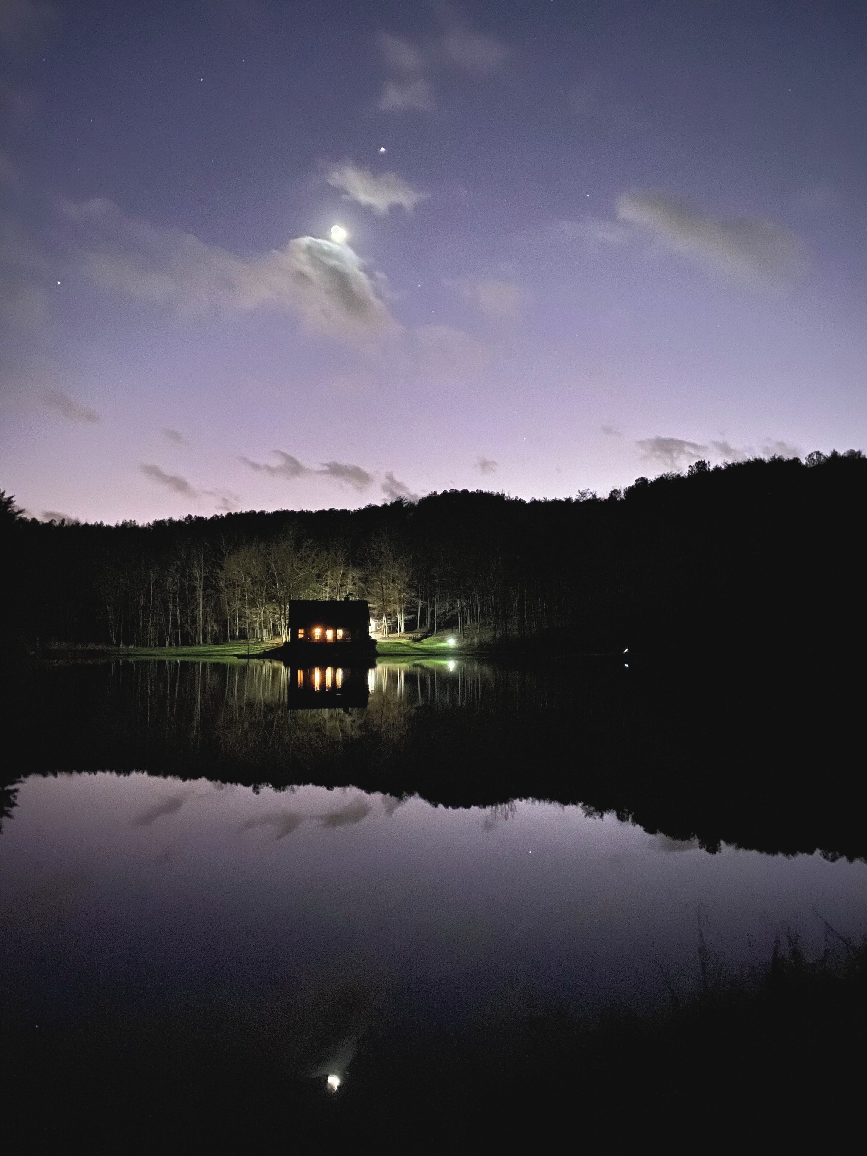 Uma casa à beira de um lago à noite, com reflexo nítido na água.