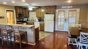 A modern kitchen with wooden cabinets, a central island with bar stools, a refrigerator, and a dining area with a table and chairs.