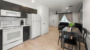 Una cocina moderna con armarios oscuros, un refrigerador blanco y un horno empotrado. Hay un comedor con una mesa y sillas negras.