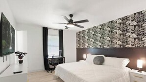 Habitación de hotel con cama, escritorio, ventilador de techo y pared con diseño de hojas.