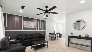 Una sala de estar moderna con un sofá negro, una mesa de centro y un comedor con una mesa y sillas.