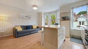 A modern kitchen with a central island, a dining area with a sofa, and large windows offering a view of the neighborhood.