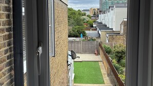 A view from a door into a courtyard with a green lawn, brick walls, and a satellite dish.
