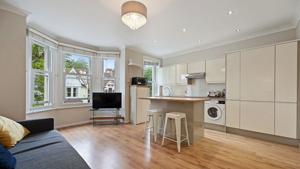 A modern kitchen with a built-in washing machine, a dining area with a grey sofa, and large windows offering a view of the neighborhood.