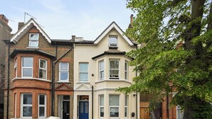 A row of terraced houses with bay windows, a narrow driveway, and a tree in the foreground.