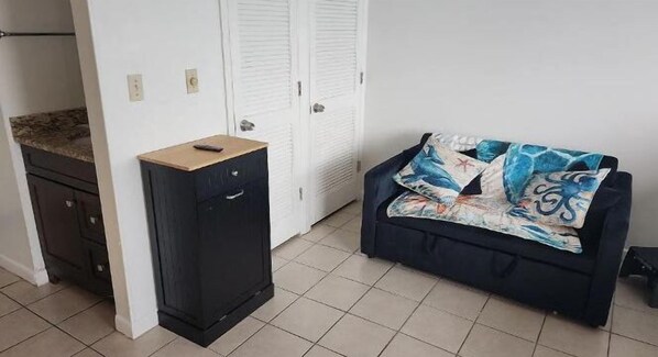 Um quarto pequeno com um armário preto, um sofá azul com um cobertor colorido e portas brancas ao fundo.