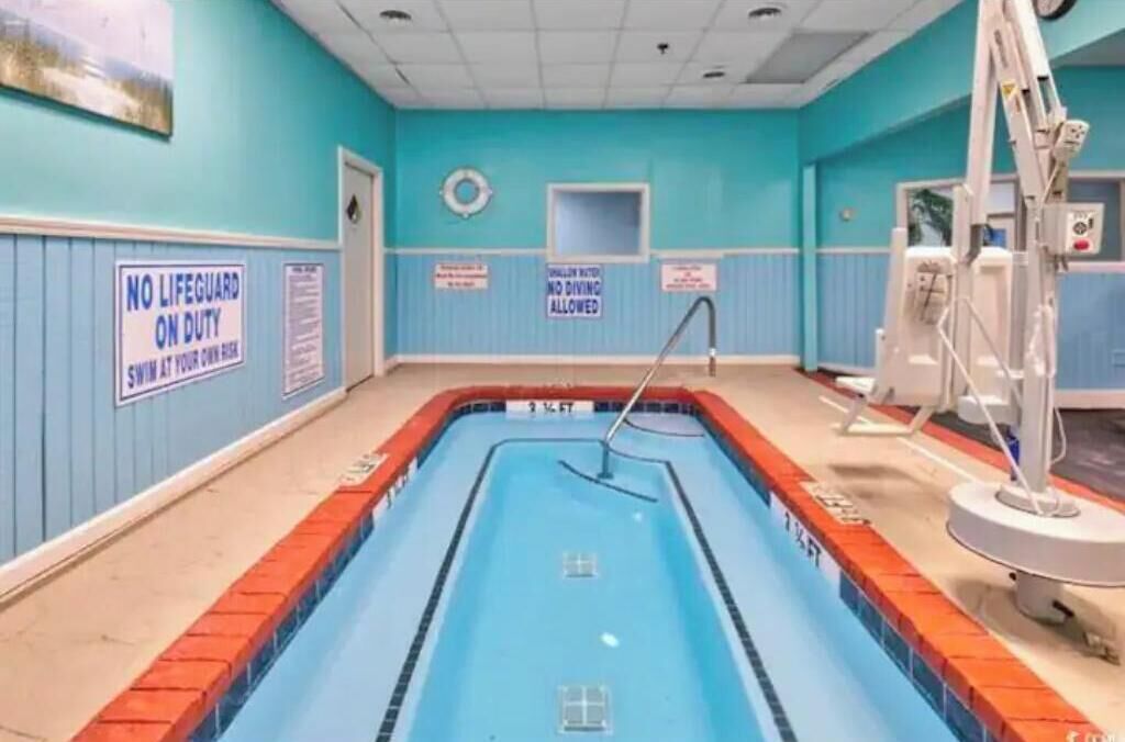 Piscina com cadeira do salva-vidas, escada e placas indicando que mergulhos não são permitidos.
