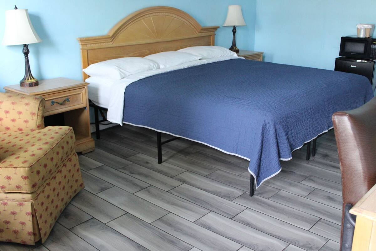 A hotel room with a bed, a nightstand, a lamp, a chair, and a television.