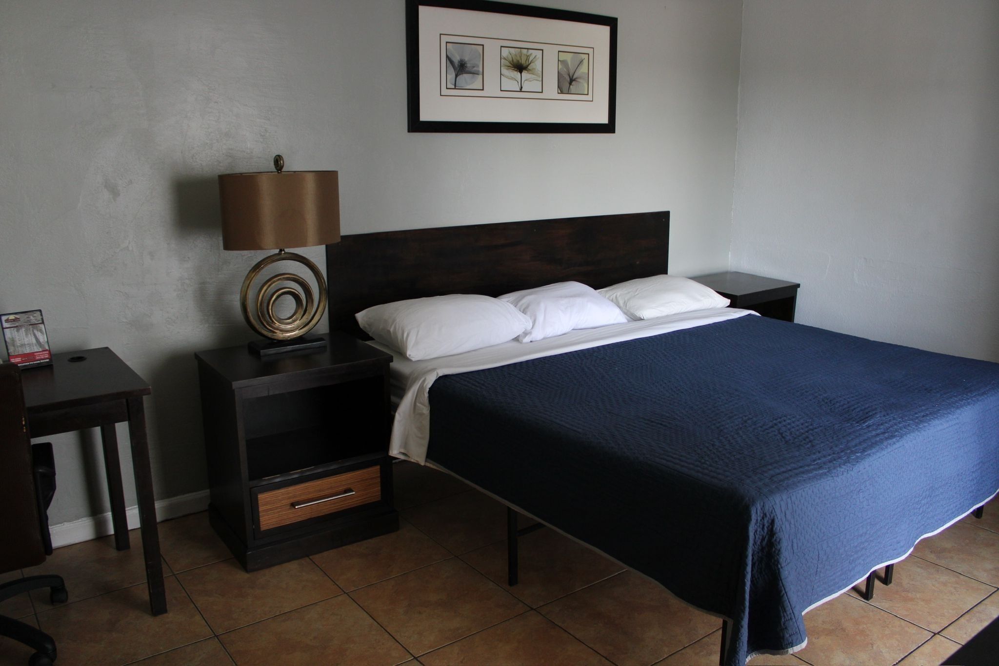 A neatly arranged bedroom with a bed, a nightstand, a lamp, and a framed picture on the wall.