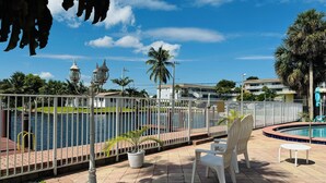 A poolside area with a view of the water, a white fence, and a few chairs and tables. - Executive Economy Lodge (Pompano Beach)