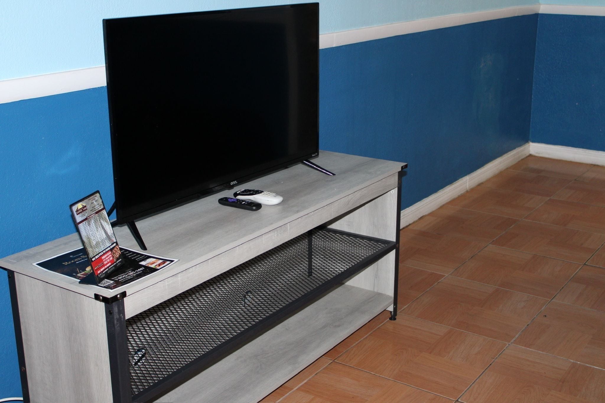 Un televisor sobre una consola gris, con un control remoto y una revista.