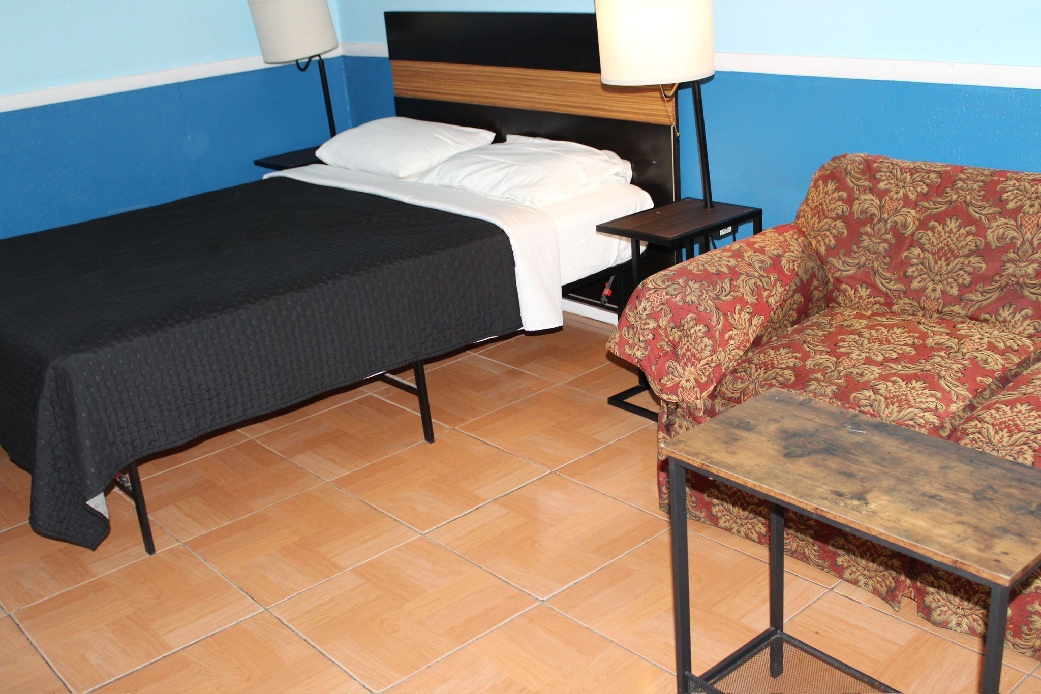 A room with a bed, a sofa, a small table, and two bedside lamps.