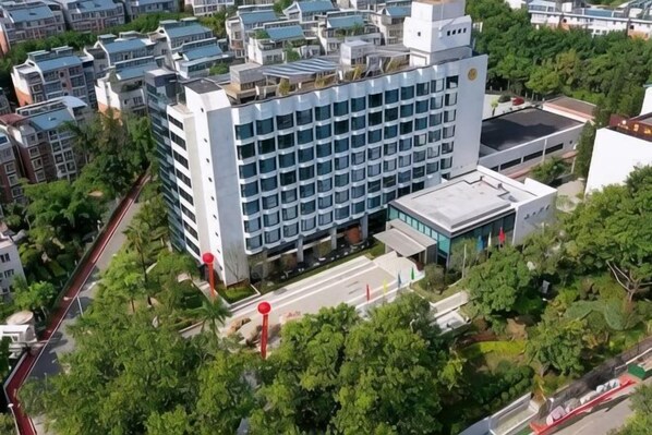 A multi-story hotel with a modern design, featuring a prominent entrance, a parking area, and surrounded by greenery.