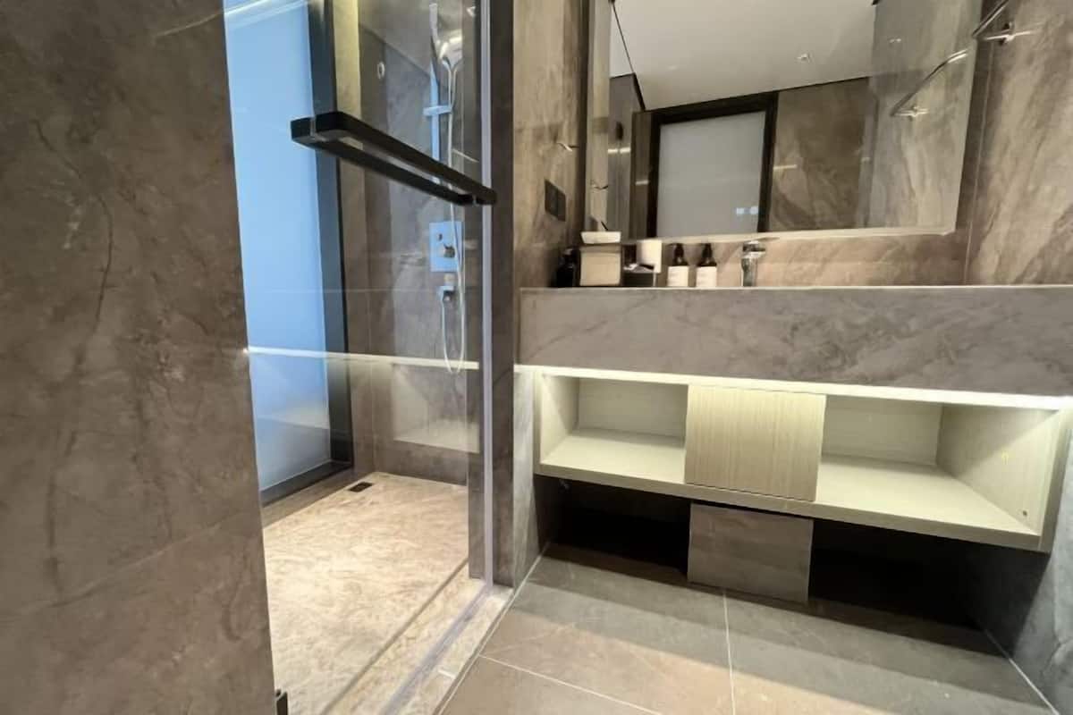 A modern bathroom with a glass shower enclosure, marble walls, and a built-in vanity with a mirror.