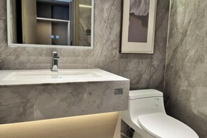 A bathroom with a marble sink, a mirror, a toilet, and a framed artwork on the wall. - Nanshan Hotel (Panzhihua)