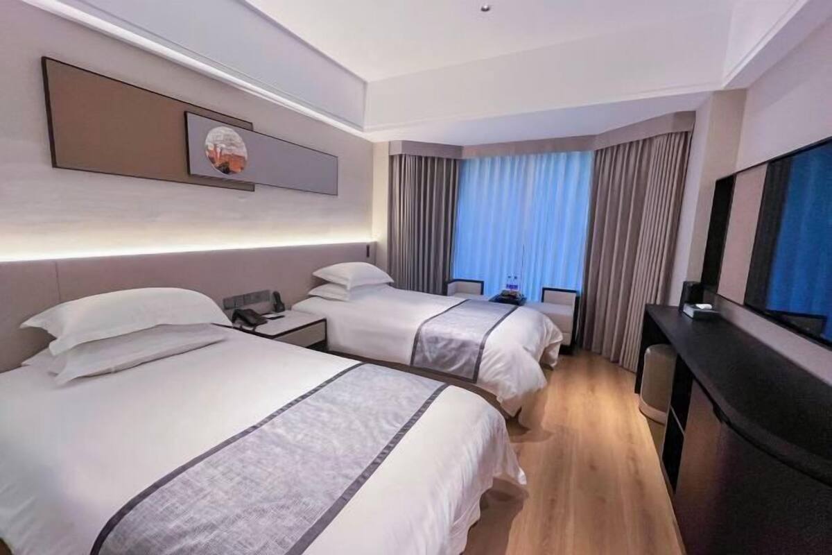 A hotel room with two beds, a desk, a TV, and a window with curtains.