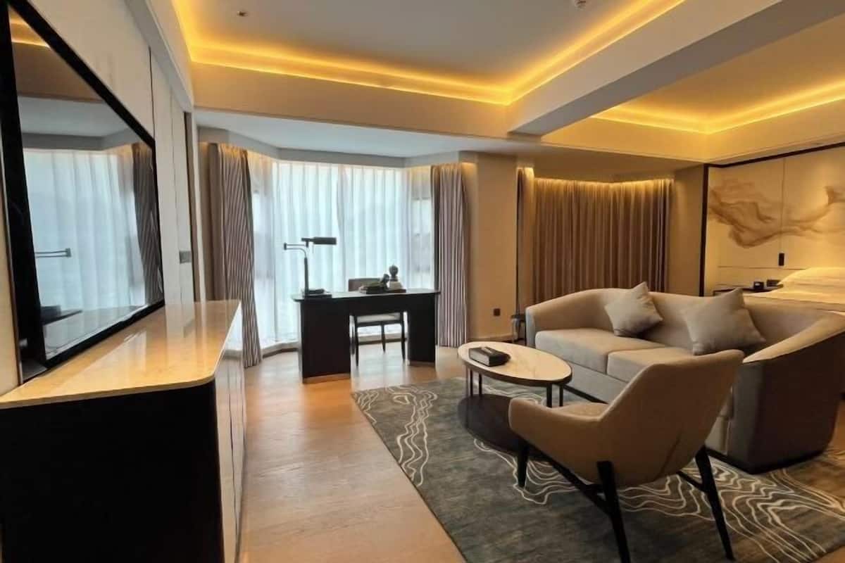 A modern hotel room with a sofa, a small table, a desk, and a large mirror.