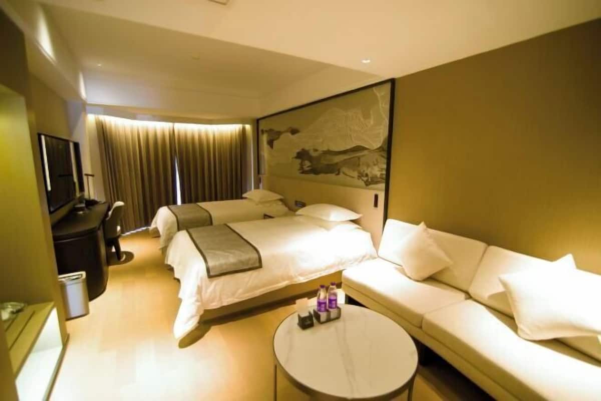 A hotel room with two beds, a sofa, a TV, and a painting on the wall.